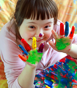 Smiling female student holds up her hands with paint on them