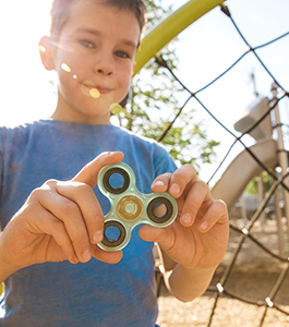 Smiling male student holds up a fidget spinner on a playground
